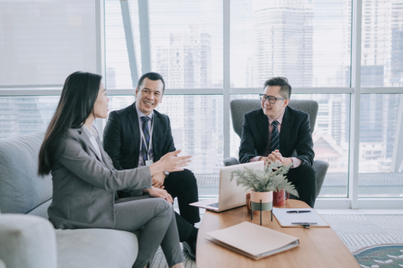 Three business professionals having a meeting in modern office setting, seated in discussion.